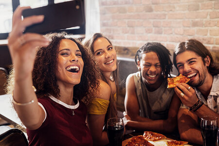 Diverse group of friends enjoying meal and taking selfie at pizza parlor