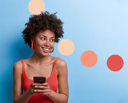 African American woman woman texting on smartphone standing up against blue wall