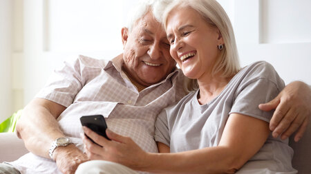 Bonding happy middle aged hoary family couple watching funny videos or photos on smartphone.
